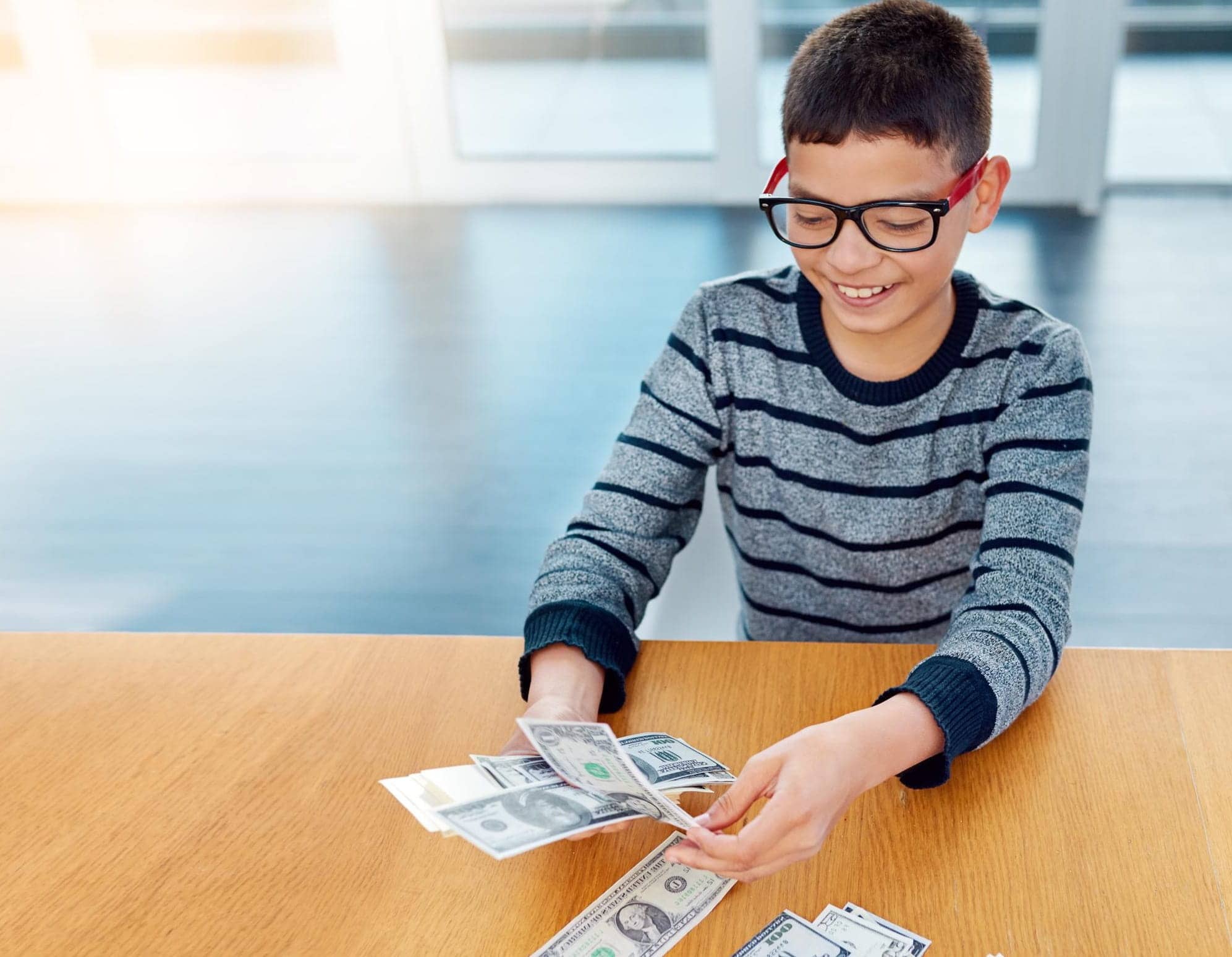 kid with glasses smiling and holding dollar bills in his hands