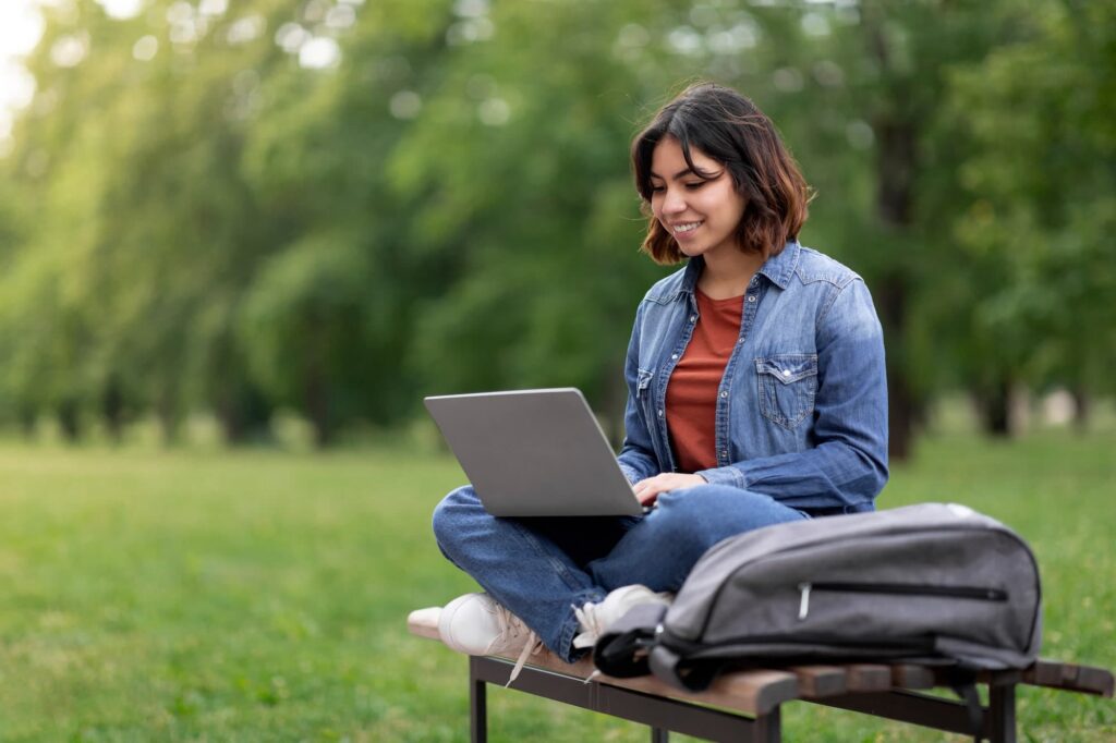 girl sitting on a bench in a park with her laptop on her lap