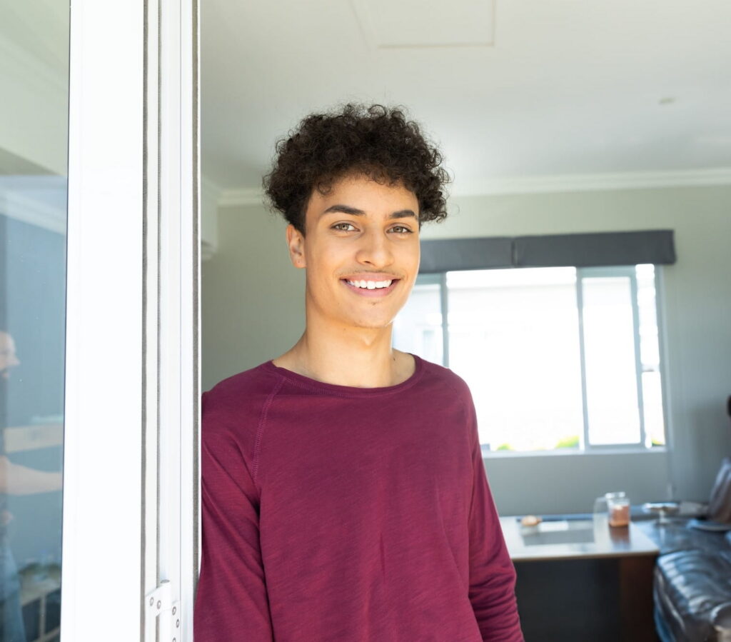 kid with curly hair standing next to a door smiling